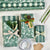 A flat-lay of wrapping paper and gift accessories on a white background, including rolls of green and white striped and floral wrapping paper, three wrapped gift boxes with bows and ribbons, a roll of clear tape, kraft gift tags, and a pinecone.