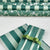 Green and white striped wrapping paper with a floral pattern, shown wrapped around a gift box tied with a green ribbon, with additional rolls of the same paper in the background.