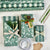 A flat-lay of wrapping paper and gift accessories on a white background, including rolls of green and white striped and floral wrapping paper, three wrapped gift boxes with bows and ribbons, a roll of clear tape, kraft gift tags, and a pinecone.